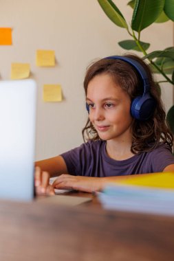 Çocuk derste müzik dinler. Kıvırcık saçlı çocuk mesafeli öğrenme ile mutlu. Dersler İnternet üzerinden yapılıyor.