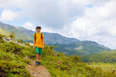 Sırt çantalı bir çocuk yaz tatilinde bir dağ çayırında yürür. Yürüyüş ve yürüyüş. Aktif sağlıklı yaşam tarzı hafta sonu yürüyüşü.