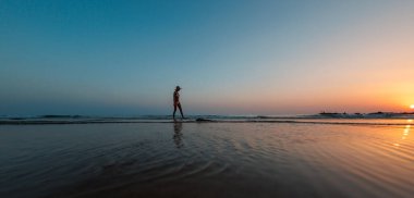 Sahilde yürüyen bir kadının silüeti. Ruhani dünyanın meditasyonu. Mutlu kız gün batımına karşı sahilde yürüyor. yan görünüm.