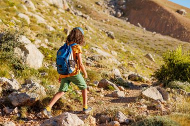 Yaz kampı. Sırt çantalı çocuk. Çocuk sırt çantasıyla dağlarda geziyor. Yüksek dağlarda yaz yürüyüşü. Bir çocuk dağ yolunda yürüyor. Türkiye.
