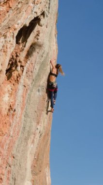 Dikey çekim. Bir kız kayaya tırmanıyor. Kaya tırmanışçısı antrenman yapıyor. Güçlü bir atlet zor bir tırmanış rotasının üstesinden gelir. Olağanüstü bir spor. Bir kadın doğada spor yapar..