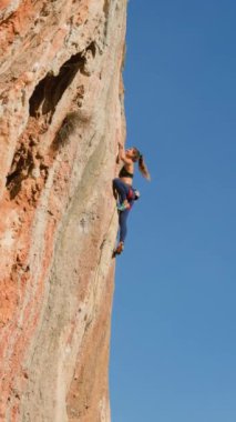 Dikey çekim. Bir kız kayaya tırmanıyor. Bir kadın doğada spor yapar. Bir dağcı kayaya tırmanma eğitimi alıyor. Güçlü bir atlet zor bir tırmanış rotasının üstesinden gelir. Sıra dışı spor.