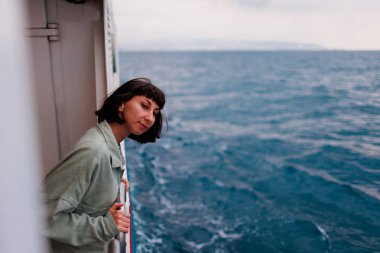 Genç bir kadın bir yolcu gemisinin güvertesinde duruyor ve batan güneşe bakıyor, yakın çekim siluetine. Genç ve güzel bir esmer yat ile seyahat ediyor. seyahat ve macera.