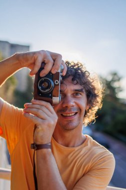 Elinde fotoğraf makinesi olan yakışıklı, şık bir gencin portresi. Bir adam eski moda bir kameranın objektifinden bakar ve fotoğraf çeker. film kamerası.