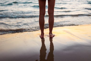 Yaz havası. Arkadan bak. Denizde bir kadın duruyor. Bacaklarını kapat. Gün batımında genç ve güzel bir kızın bacakları. Hafta sonu doğa gezisi. Kumsalda dinlenmek.