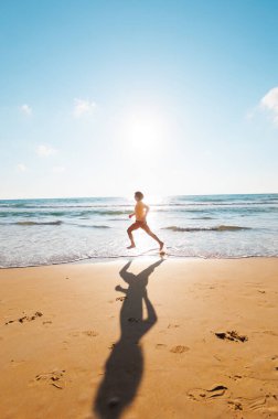 Aktif adam koşuyor. Sağlıklı bir yaşam tarzı. Bir adam deniz kenarında yalınayak koşuyor. Genç bir koşucu şafakta boş bir plaj boyunca koşar. Denize yakın koş..