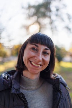 Kısa esmer saçlı, neşeli, güzel bir kız. Açık havada poz vermek. Deri ceket, sokak tarzında yakın moda portresi..