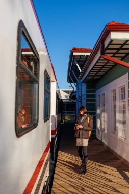 Elinde telefon olan genç ve güzel bir kız trenin yanında duruyor. Yolculuğun tadını çıkarıyorum. Seyahat kavramı.