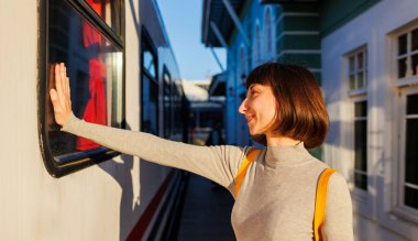Genç gezgin platformda duruyor ve trendeki birine el sallayarak veda ediyor. Gitmeden önce hoşça kal de. seyahat ve macera.