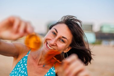 Mutlu kadın gülümsüyor ve sahilde eğleniyor. Genç ve güzel bir kızın yaz portresi. Güneş gözlüklü genç kız. Kız yaz tatilini denizde geçiriyor. Kumsalda dinlenmek..