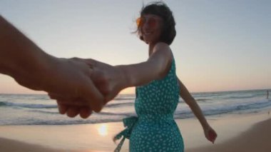 Beni takip edin. Mutlu genç kadın adamın elini tutuyor. Elbise giymiş güzel bir kız sahilde yürüyor, bir erkeğin elini tutuyor, romantik bir yürüyüş. Sahilde yürü..