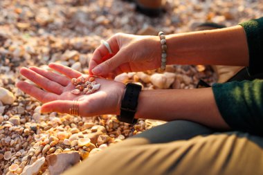 Kız sahilde dinleniyor. Bir kız sahilde oturur ve elinde çeşitli kabuklar toplar. Yakın plan kabuklu eller. dinlenme ve meditasyon.