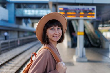 Sırt çantalı bir kız. İstasyonda şapkalı güzel ve genç bir kızın portresi. Paltolu ve şapkalı genç bir kadın istasyon platformunda duruyor. Maceralar ve seyahat.