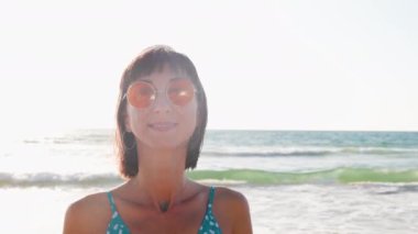 Yaz havası. Sahildeki kız. Güneş gözlüklü mutlu genç kız sahilde dinleniyor. Yüzünüzü kapatın. Mutlu kadın. Kız kumsalda duruyor. Kumsalda dinlenmek..