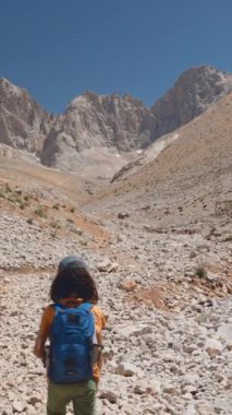 Dikey çekim. Dağlarda mutlu bir çocuk. Sırt çantalı bir çocuk dağlarda bir patika boyunca yürüyor. Dağlarda yürüyüş..