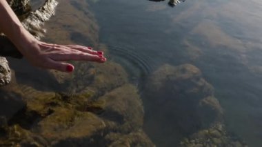 Kadının eli sakin su yüzeyine değiyor. Doğada huzur ve zen hissi.