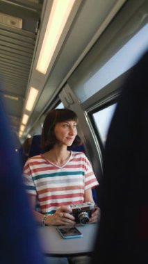 Dikey çekim. Tren yolculuğu. Genç bir kadın tren yolculuğundan zevk alıyor ve kamerasıyla güzel turistik noktaların fotoğraflarını çekiyor. Film kamerası. Kız film kamerası kullanıyor..
