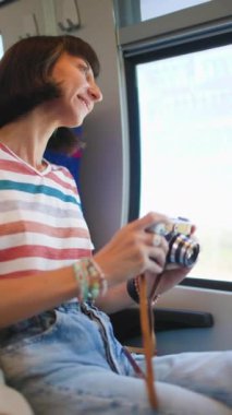 Dikey çekim. Tren yolculuğu. Genç bir kadın tren yolculuğundan zevk alıyor ve kamerasıyla güzel turistik noktaların fotoğraflarını çekiyor. Film kamerası. Kız film kamerası kullanıyor..