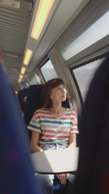 Dikey çekim. İyi yolculuklar. tren yolcusu. Tren yolculuğu. Genç ve güzel bir kadın tren yolculuğundan zevk alıyor, pencerenin kenarında oturuyor ve pencereden dışarı bakıyor..
