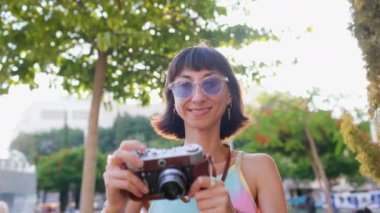 Elinde kamera olan kadın fotoğrafçı şehir caddesinde fotoğraf çekiyor. Genç bir bayan fotoğrafçı objektife nişan alır ve çekim sürecinden zevk alır. ön görünüm.