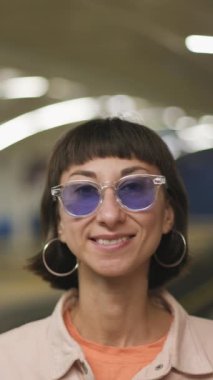 Dikey çekim. Gözlüklü genç bir kızın yüzü. Kız metro istasyonunda duruyor..