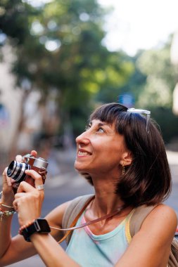 Kameralı kadın fotoğrafçı dışarıda fotoğraf çekiyor. Kız şehirde dolaşıp kamerayla fotoğraf çekiyor. Şehirde film kamerası olan genç bir kız. Kız fotoğraf çekiyor. seyahat ve macera.