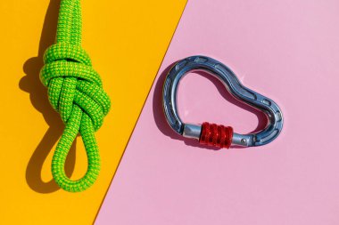 rope with a secure knot and a carabiner lies on a colored background. Equipment for rock climbing and mountaineering. reliable connection. Safety rope. concept of reliability and strength.
