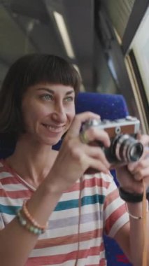 Dikey çekim. Tren yolculuğu. Kız fotoğrafçı. Şık elbiseli genç kız tren yolculuğunun tadını çıkarıyor ve kamerasıyla güzel turistik yerlerin fotoğraflarını çekiyor. Film kamerası. Kız film kamerası kullanıyor..