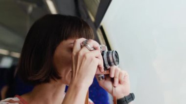 Trendeki kız. Genç bir kız tren yolculuğu sırasında pencereden güzel bir manzaranın fotoğrafını çekmek için kamera kullanıyor. Çekici bir kız trenle seyahat eder. film kamerası.