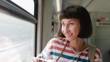Trendeki kız. Genç bir kız tren yolculuğu sırasında pencereden güzel bir manzaranın fotoğrafını çekmek için kamera kullanıyor. Çekici bir kız trenle seyahat eder. film kamerası.
