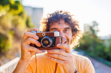 Elinde fotoğraf makinesi olan yakışıklı, şık bir gencin portresi. Bir adam eski moda bir kameranın objektifinden bakar ve fotoğraf çeker. film kamerası.