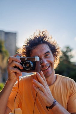 Elinde fotoğraf makinesi olan yakışıklı, şık bir gencin portresi. Bir adam eski moda bir kameranın objektifinden bakar ve fotoğraf çeker. film kamerası.