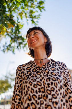 Leopar desenli bluz giyen neşeli genç bir kadın bir yaz günü sokakta yürür. Şehirde yürü..