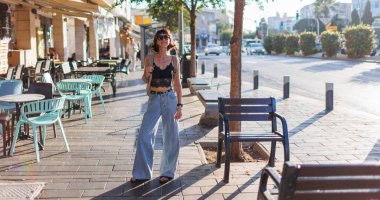 Şık giyinmiş bir kız şehirde yürümekten hoşlanıyor. Gülümseyen genç ve neşeli bir kadın. Bir yaz gününde yürümek.