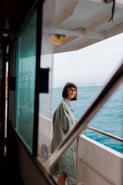 Genç bir kadın bir yolcu gemisinin güvertesinde duruyor ve batan güneşe bakıyor. Genç ve güzel bir esmer, güzel bir mavi denizin arka planında bir yatla seyahat ediyor. seyahat ve macera.
