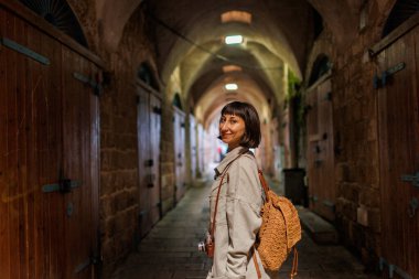 Sırt çantası ve kamerası olan şık bir kız eski şehrin caddesinde duruyor. Maceralar ve seyahat.