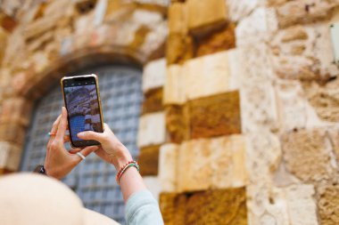 Genç bir kadın telefonuyla fotoğraf çekiyor. Bir kız eski Arco-Israel şehrini ziyaret ediyor. Mutlu turistler. Seyahat ve tatil yaşam tarzı kavramı