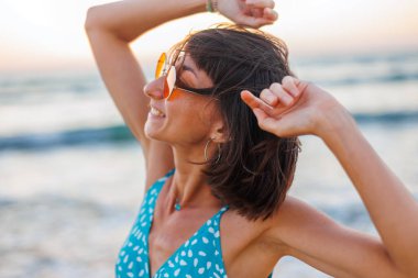 Mutlu kadın gülümsüyor ve sahilde eğleniyor. Genç ve güzel bir kızın yaz portresi. Güneş gözlüklü genç kız. Kız yaz tatilini denizde geçiriyor. Kumsalda dinlenmek..