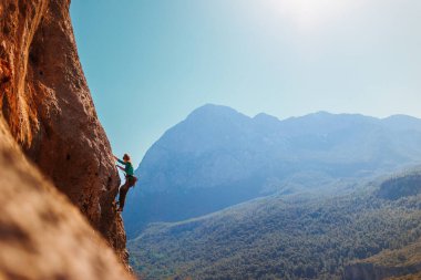 Kız tırmanışçı bir kayaya tırmanır orman ve dağların arka planına karşı. Kaya tırmanışçısı zor bir yolda dinleniyor. Türkiye 'de kaya tırmanışı.