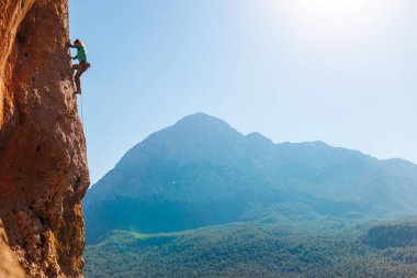 Kız tırmanışçı bir kayaya tırmanır orman ve dağların arka planına karşı. Kaya tırmanışçısı zor bir yolda dinleniyor. Türkiye 'de kaya tırmanışı.