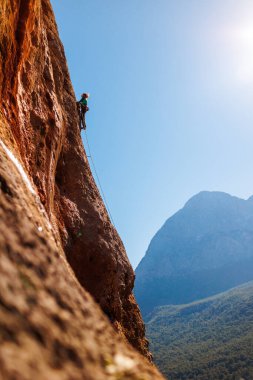 Kız tırmanışçı bir kayaya tırmanır orman ve dağların arka planına karşı. Kaya tırmanışçısı zor bir yolda dinleniyor. Türkiye 'de kaya tırmanışı.