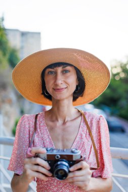 Genç bir bayan gezgin şehirde analog bir kamera kullanarak fotoğraf çekiyor. Kameralı kadın fotoğrafçı dışarıda fotoğraf çekiyor.