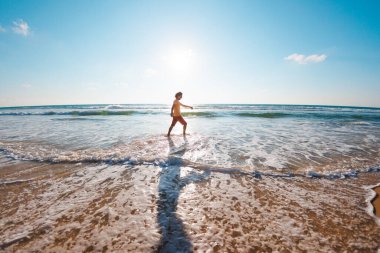 Mutlu, güneşli bir günde okyanus kıyısında dinlenen adam. Genç bir adam dalgalar boyunca kumlu bir sahil boyunca yürüyor..