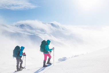 Kış aktivitesi. Karda kar ayakkabılarıyla yürüyen iki kadın, kış yürüyüşü yapan iki kişi, kışın dağlarda yürüyüş yapan iki kişi.