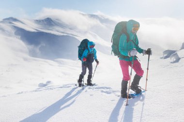Dağcılar karda dağa tırmanırlar. Kış dağcılığı. Kar ayakkabılı iki kız karda yürür. Dağcılık ekipmanları. Kışın dağlarda yürüyüş..