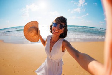 Neşeli kadın bir plaj tatilinde fotoğraflanır. Kumsalda tatildeyken fotoğraf çekilirken akıllı telefon kamerasına gülümseyen mutlu kız. Kız selfie çekiyor..