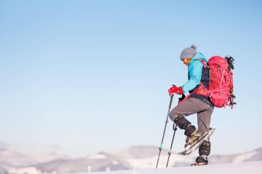 Dağlara tırmanan. Sırt çantalı ve kar ayakkabılı bir kız karda yürüyor. Dağlarda kış yürüyüşü.
