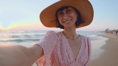 Sahilde selfie. Kumsalda dinlenen ve selfie çeken gülümseyen kız. Şapkalı güzel kız. Plajda pembe elbiseli bir kız..