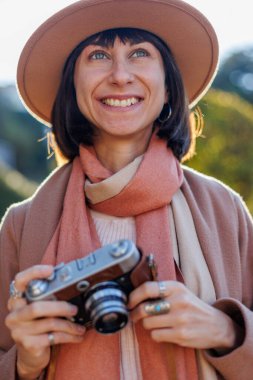 Modaya uygun bir görünüş. Elinde kamera olan genç bir kadın cadde boyunca yürüyor. Kameralı hippi turist kadın. Yaşam tarzı konsepti. film kamerası.