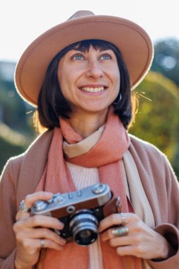 Modaya uygun bir görünüş. Elinde kamera olan genç bir kadın cadde boyunca yürüyor. Kameralı hippi turist kadın. Yaşam tarzı konsepti. film kamerası.